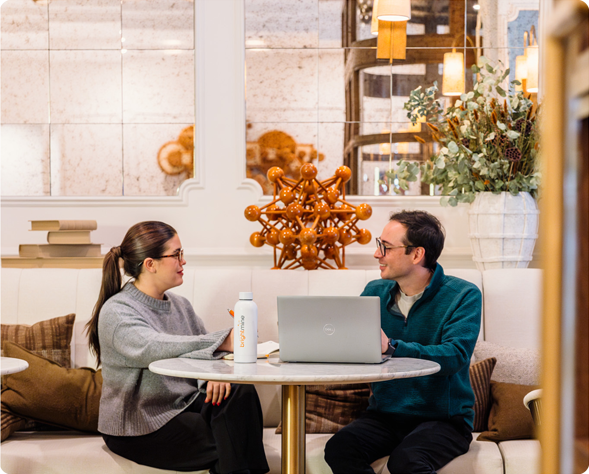 Two individuals seated at a table, collaborating over a laptop